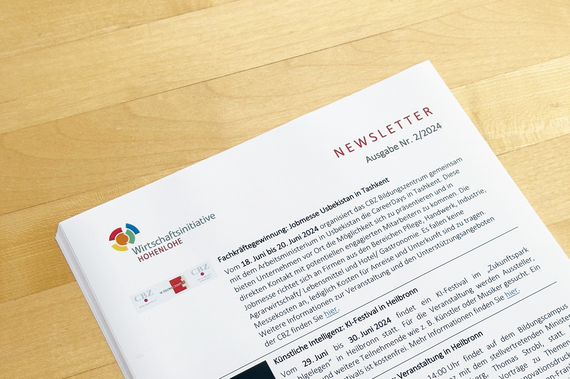 Ein Newsletter der Wirtschaftsinitiative Hohenlohe liegt auf einem Holztisch, mit dem Titel "Newsletter Ausgabe Nr. 2/2024".