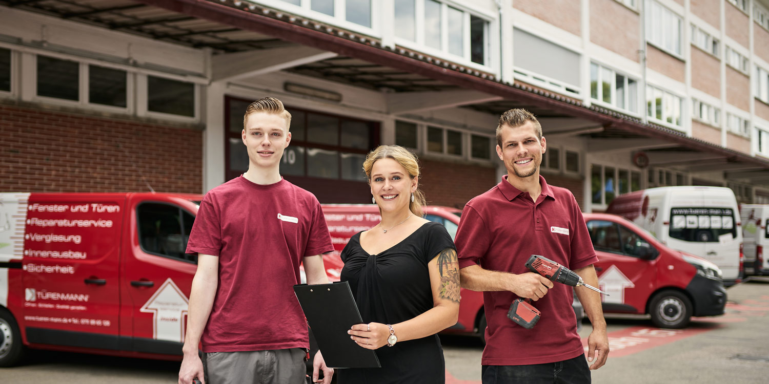 Ein Service-Team steht lächelnd vor Firmenfahrzeugen mit Werkzeug und Klemmbrett bereit für Fensterinstallationen.